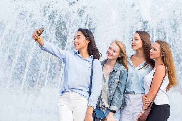 Un grupo de jóvenes chicas atractivas de los estudiantes se toma una selfie en el fondo de una hermosa fuente —  Fotos de Stock