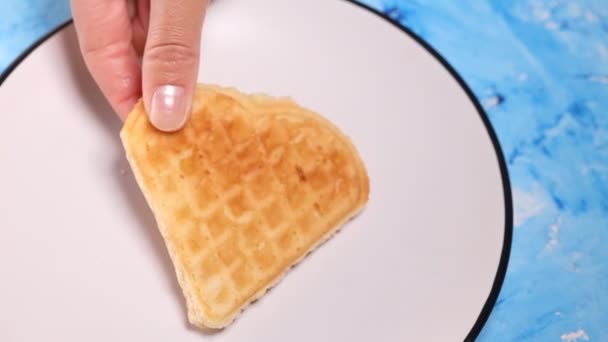 Close-up uma mão de mulheres expõe waffles frescos em uma chapa branca em um fundo azul — Vídeo de Stock