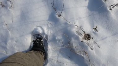 Siyah ayakkabılı bir adam kışın beyaz karda yürür.