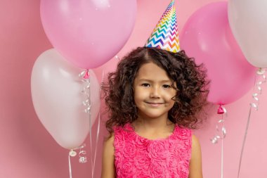 Şenlik kıyafetleri içinde elinde balonlarla küçük bir çocuk.