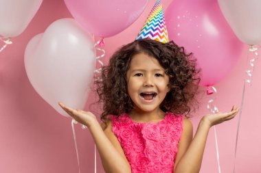 Şenlik kıyafetleri içinde elinde balonlarla küçük bir çocuk.