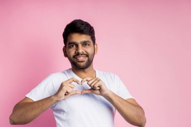 Pembe arka planda duran yakışıklı Hintli adamın portresi.