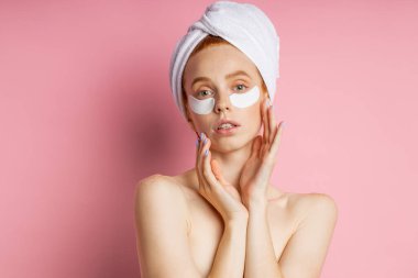 Göz altı bantlı genç bir kadın pembe arka planda izole edilmiş.