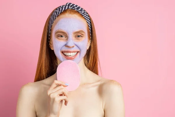 Wanita cantik dengan masker wajah di latar belakang merah muda — Stok Foto