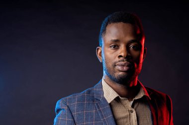 Stüdyoda karanlıkta poz veren yakışıklı adam. Sakallı, kareli takım elbiseli, siyah arka planda ciddi bir ifadeye sahip Afro-Amerikan iş adamının yakın plan portresi..