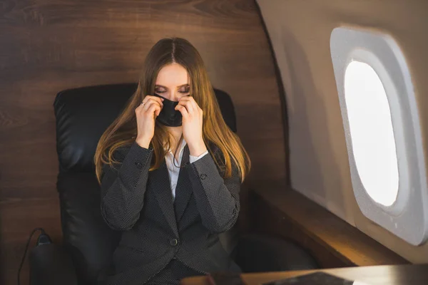 Jeune belle femme d'affaires assise dans un avion avec un masque médical noir lors d'une pandémie de coronavirus — Photo