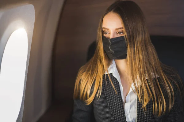 Jeune belle femme d'affaires assise dans un avion avec un masque médical noir lors d'une pandémie de coronavirus — Photo