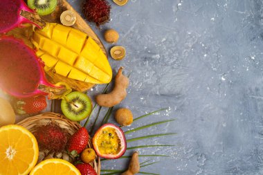 Bir takım papaya, ejderha meyvesi, rambutan, tamarind, mango, çarkıfelek meyvesi, kivi, portakal, çilek, yeşil yapraklar ve fotokopi alanı. Düz konum, üst görünüm yaz kompozisyonu.