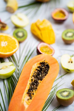 Çeşitli olgun sulu taze tropikal yaz mevsimsel meyveleri ve beyaz arka planda tropikal yapraklar. Egzotik Asya meyveleri. Masada dilimlenmiş meyve. Seçici odaklanma. Dikey çekim.