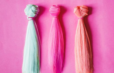 Colorful dolls hair on pink background clipart