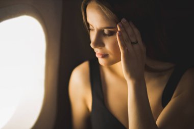 Güzel, yorgun bir kızın pencerede otururken, kafasına dokunurken, stres, baş ağrısı ve migren çekerken yakın plan çekimi. Genç kadın uçmaktan korkuyor. Uçma korkusu, acı, havacılık fobisi.