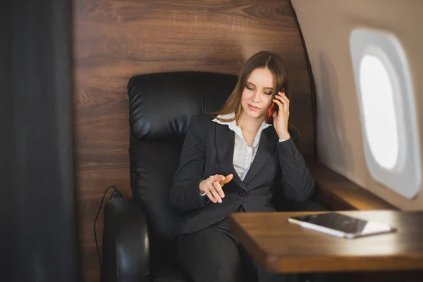 Beautiful rich woman in first class plane. Young businesswoman in formal wear sitting in private jet, talking on cell phone during flight.