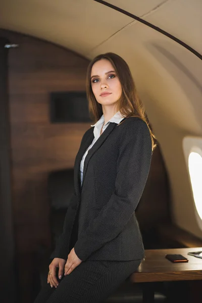 Traveling at first class. Flight with comfort. Beautiful successful caucasian young lady wearing stylish black suit in private aircraft. Business, success, travel concept.