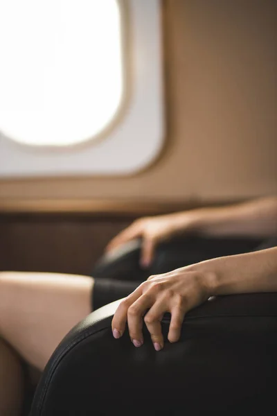 Cropped vertical shot of businesswoman with flight fear in private jet. Selective focus of terrified woman sitting clutching the arms of the chair in private plane. Aerophobia concept.