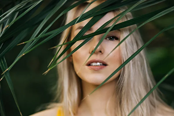 可爱的高加索金发女郎 有着洁白的皮肤 自然的妆容 美丽的眼睛 站在热带树叶的后面 垂直射击 护肤概念 — 图库照片