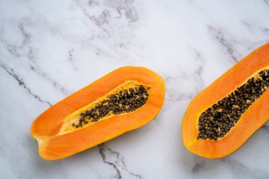 Olgunlaşmış papaya meyvelerinin yarısının tohumlarla yakınlaştırılması. Beyaz mermer masada olgun taze papaya meyvesi. Üst Manzara. Yatay çekim. Vejetaryen diyeti, egzotik meyveler, gıda konsepti.