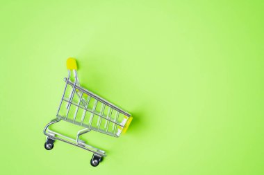 Boş metal alışveriş arabası pembe yeşil arka planda izole edilmiş metin veya tasarımın için fotokopi alanı var. Üst manzara, düz yatış. Süpermarket, alışveriş merkezi, market, alışveriş, satış kavramı.