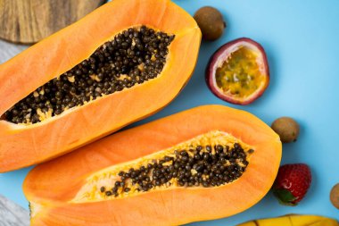 Olgun papaya meyvesi mavi arka planda yarı yarıya izole edilmiş. Tohumlu taze papaya meyvelerinin üst görüntüsü. Vejetaryen diyeti, egzotik meyve kavramı. Yatay çekim, düz yatış.