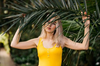 Güzel sarışın bir kadının yatay portresini kapat. Egzotik bir ormanda, palmiye ağacının yeşil uzun yapraklarıyla.