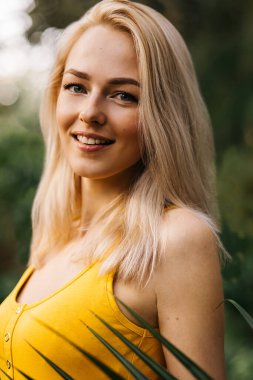 Sahilde palmiye ağacının yanında duran, parlak mayo giyen ve tropik adada dinlenen mutlu, güzel, lüks sarışının dikey portresini kapat. Tatil, seyahat, yaz.