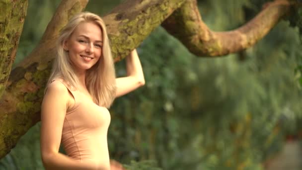 나무 옆에 있는 이국적 인 숲 속에 있는 아름다운 금발의 소녀의 모습 — 비디오