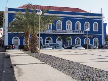 Cape Verde 'deki Sao Vicente adasındaki Afrika Mindelo şehir meydanında beyaz pencereli ve palmiye ağaçlı koyu mavi bir bina.