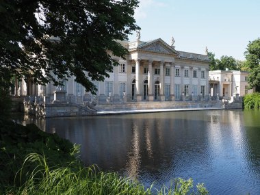Palace on isle reflected in water behind bough at lake in baths park in Warsaw european capital city of Poland, clear blue sky in 2019 warm sunny spring morning day on July.