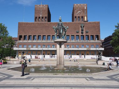 OSLO, NORway, Temmuz 2019: Ostlandet ilçesinde Avrupa 'nın başkentinin ana meydanındaki belediye binasının önündeki heykel ve çeşme manzarası güneşli yaz gününde açık mavi gökyüzü.