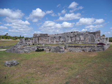 Meksika 'nın Quintana Roo kentindeki Tulum kentindeki Maya tapınağının kalıntıları çimenli arazide, 2018' in ılık kış gününde bulutlu mavi gökyüzü..