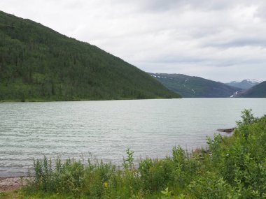 Norveç 'in Nordland ilçesindeki Avrupa Svartisen buzulu yakınlarında Svartisvatnet Gölü' nün dağ sıraları ve kıyıları, Temmuz 'un soğuk yaz günü 2019' da bulutlu gökyüzü.