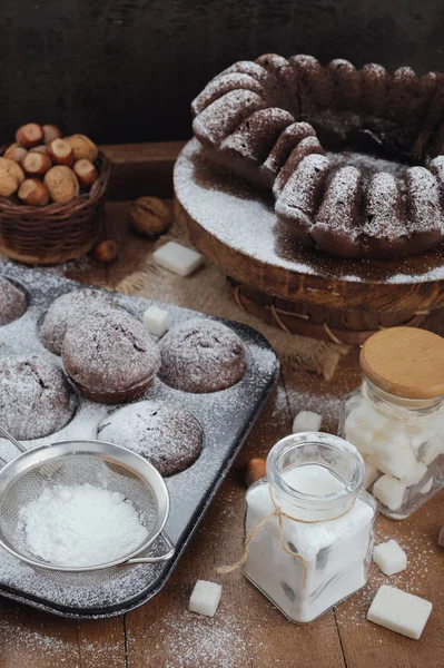 Chokolate cake and cupcakes with powdered sugar on rustic table — Stock Photo, Image