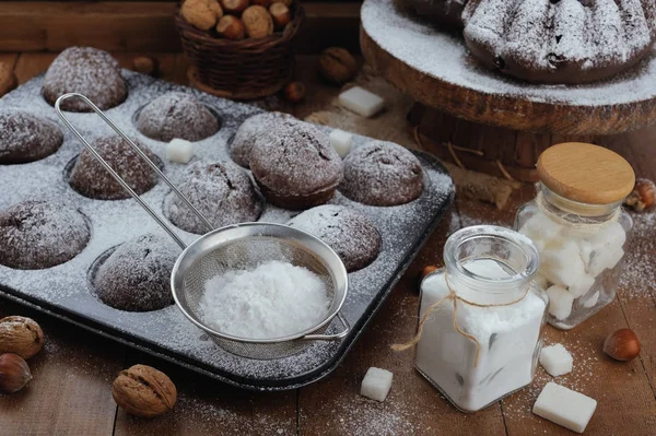 Bolo de chocolate e cupcakes com açúcar em pó na mesa rústica — Fotografia de Stock