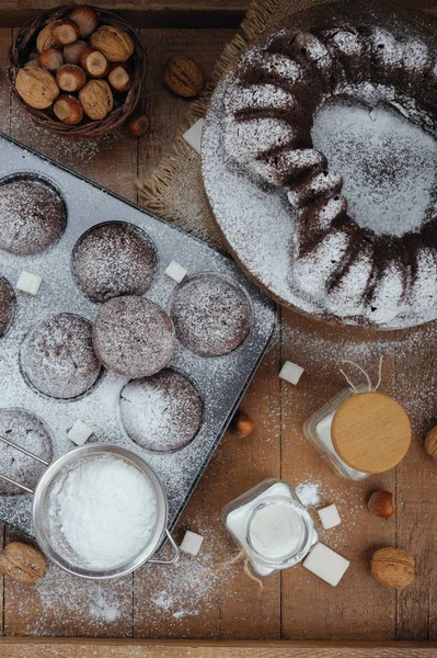 Bolo de chocolate e pequenos cupcakes com açúcar em pó na mesa rústica — Fotografia de Stock