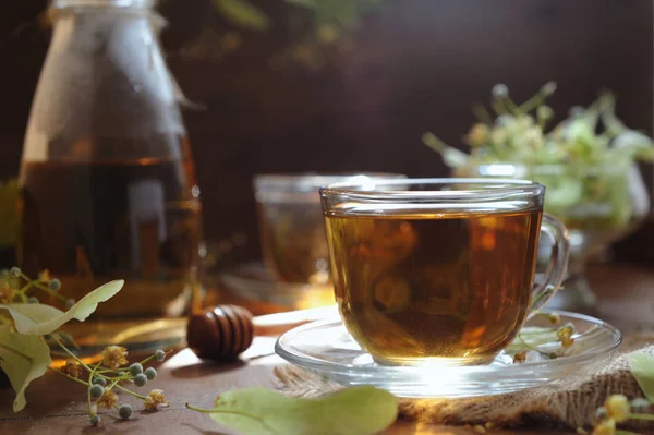 Cups of linden tea with linden flowers on wooden background in sunshine light