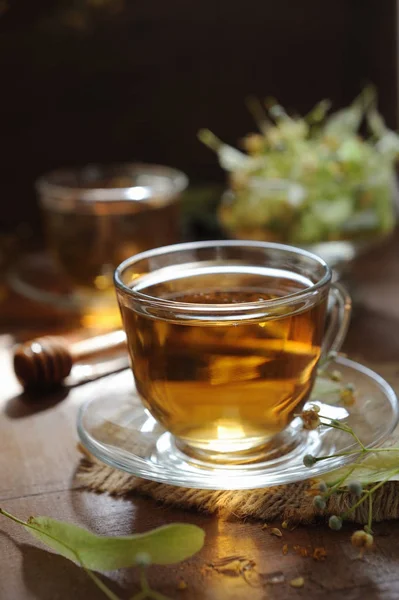 Cups of linden tea with linden flowers on wooden background in sunshine light