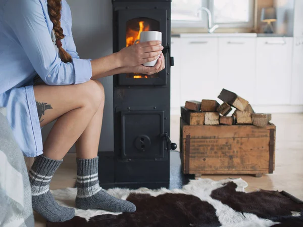 暖炉のそばにコーヒーを片手に家に立つ若い女性 木造客室内 — ストック写真