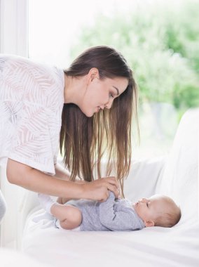 Home portrait of a young happy smiling mother with three months old baby daughter. Motherhood concept