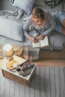Young blonde woman reading paper book story at home in living room. View from above. Christmas concept