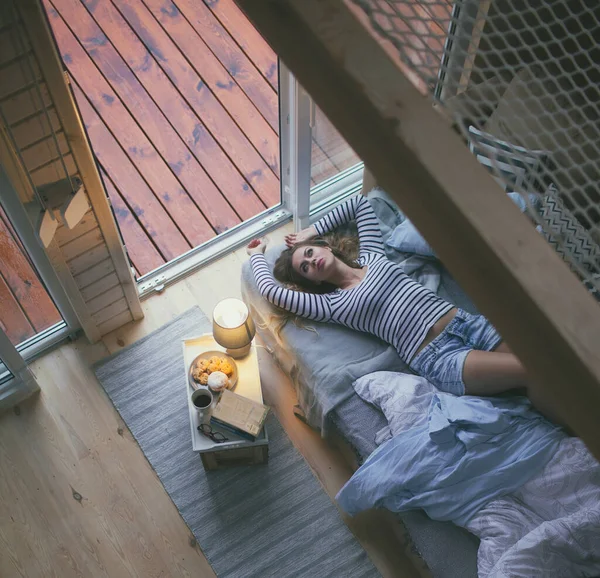 Young Woman Wearing Shorts Lying Bed Window Cozy Wooden Cabin — Stok fotoğraf