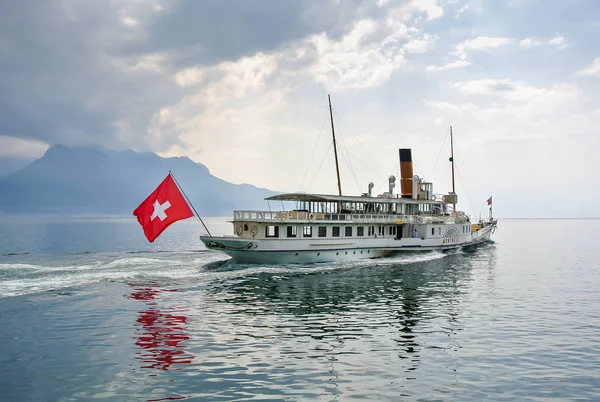 Beyaz bir gemi, İsviçre bayrağı taşıyan bir gemi ayna gölünde yüzüyor.