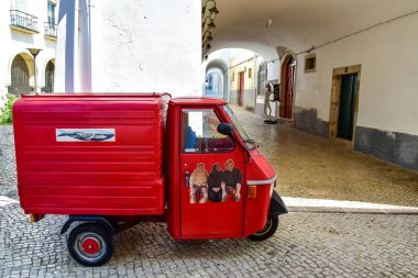 Üç tekerlekli küçük bir kırmızı kamyon caddeye park etmiş..
