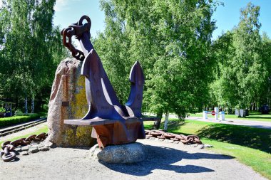 A monument of a large rusty anchor with a chain and boulders.