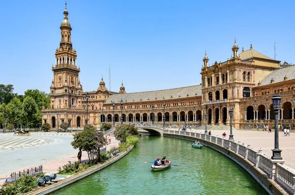 Seville, İspanya - İspanya Meydanı, neo-Berberi tarzı kentsel bir topluluk, sayısız kemerli açık kahverengi binalar, yeşil suyla dolu bir kanal boyunca yelken açan insanlar, yaz öğleden sonraları.