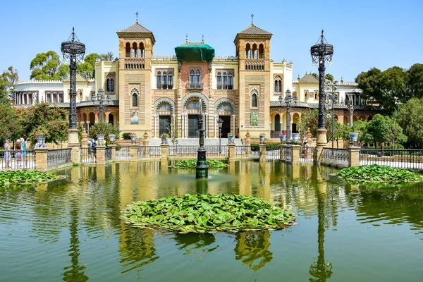 Seville, İspanya - Maria Louise Parkındaki Arkeoloji Müzesi Pavyonu, bej renkli bir bina, ön planda yeşil zambak yapraklı bir gölet, mavi gökyüzü, yaz öğleden sonra.