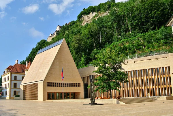 Vaduz, Lihtenştayn - Prenslik Meclisi 'nin oturduğu Lantag' in yeni binası, yeşil ağaçlarla kaplı bir arka planda sarı-bej tuğla bina, mavi gökyüzü.