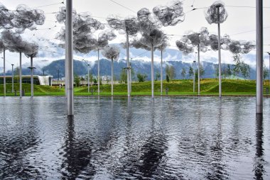 Wattens, Avusturya - 09.09.2916: Swarovski Kristal Müzesi, çiçeğe benzeyen uzun demir sütunların yer aldığı bir su birikintisi ile arka planda yeşil tepeler ve dağlar yer almaktadır..