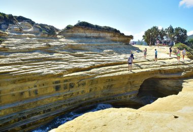 Sidari / Korfu, Yunanistan - 07 / 18 / 2018: Canal D 'Amour, kumtaşı kayalıkları, turistlerin üzerinde yürüdüğü sarı-bej kaya katmanları, suyla kaplı bir yarık, yaz öğleden sonra mavi gökyüzü.