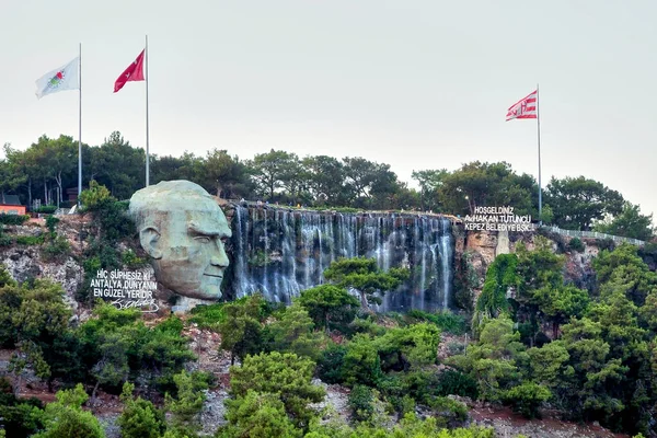 Antalya, Türkiye - 08.22.2018: Mustafa Kemal Atatürk heykeli ve şehir ormanının girişinde yapay bir şelale, bir gözlem güvertesi, büyük bir taş kafa ve bir kaya üzerindeki ağaçlar.