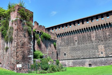 Milan, İtalya - Castello Sforzesco ya da Sforza Kalesi, kiremit tuğlalardan yapılmış kale duvarları, yeşil bitkilerle kaplı, kalenin önündeki çimenler, mavi gökyüzü.