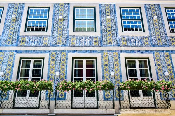 Lizbon, Portekiz - 07.23.2019: Portekiz azulejo fayanslarıyla döşenmiş şehir evi, beyaz ve sarı desenli mavi, beyaz pencere ve kapılar, pembe çiçeklerle süslenmiş balkon çitleri.